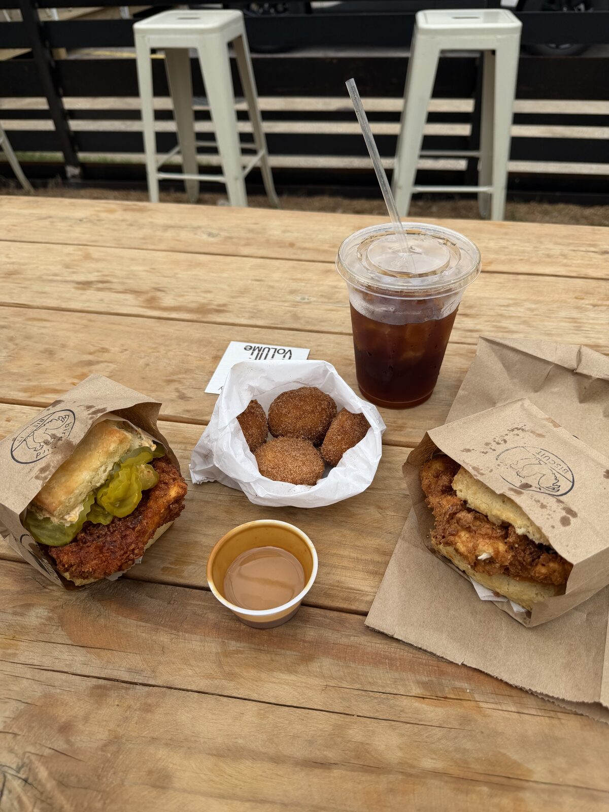 Two biscuits, donut holes, an iced cold brew, and a small cup of spicy maple aioli on a picnic table at Bird Bird Biscuit in Austin, Texas