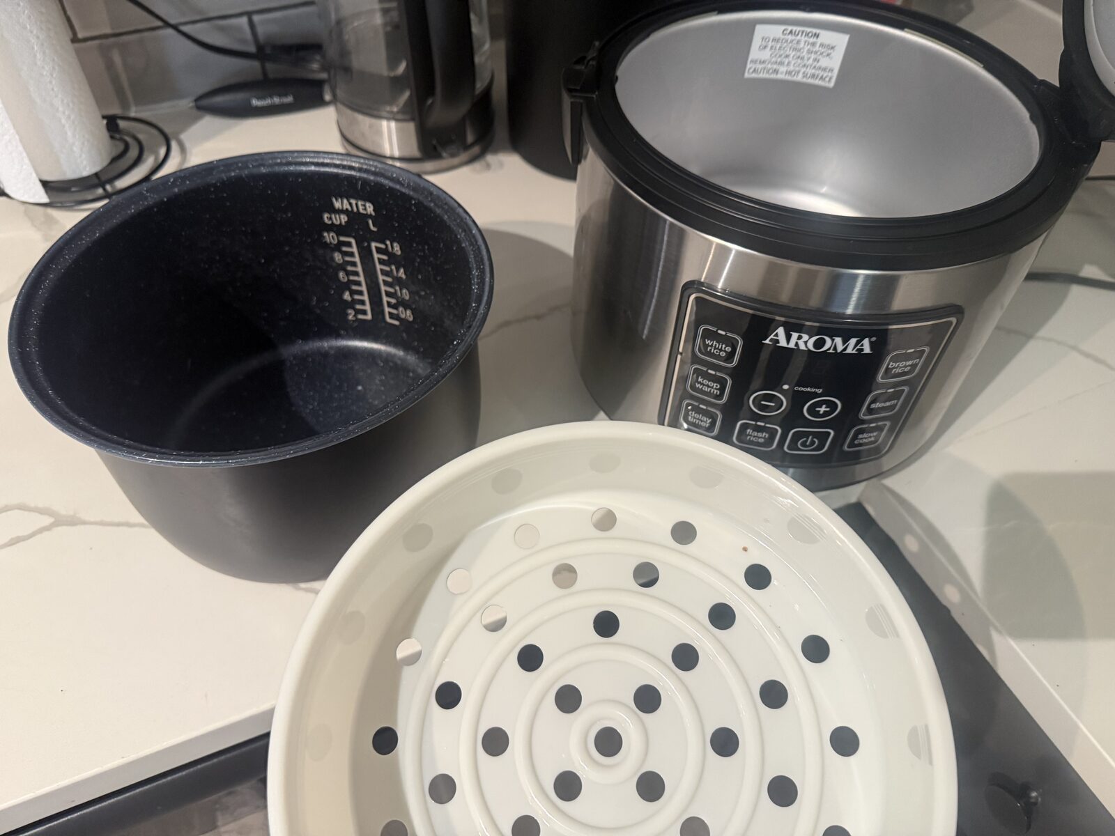 Aroma rice cooker with the inner pot, steam tray, and lid laid out on the counter ready for rice