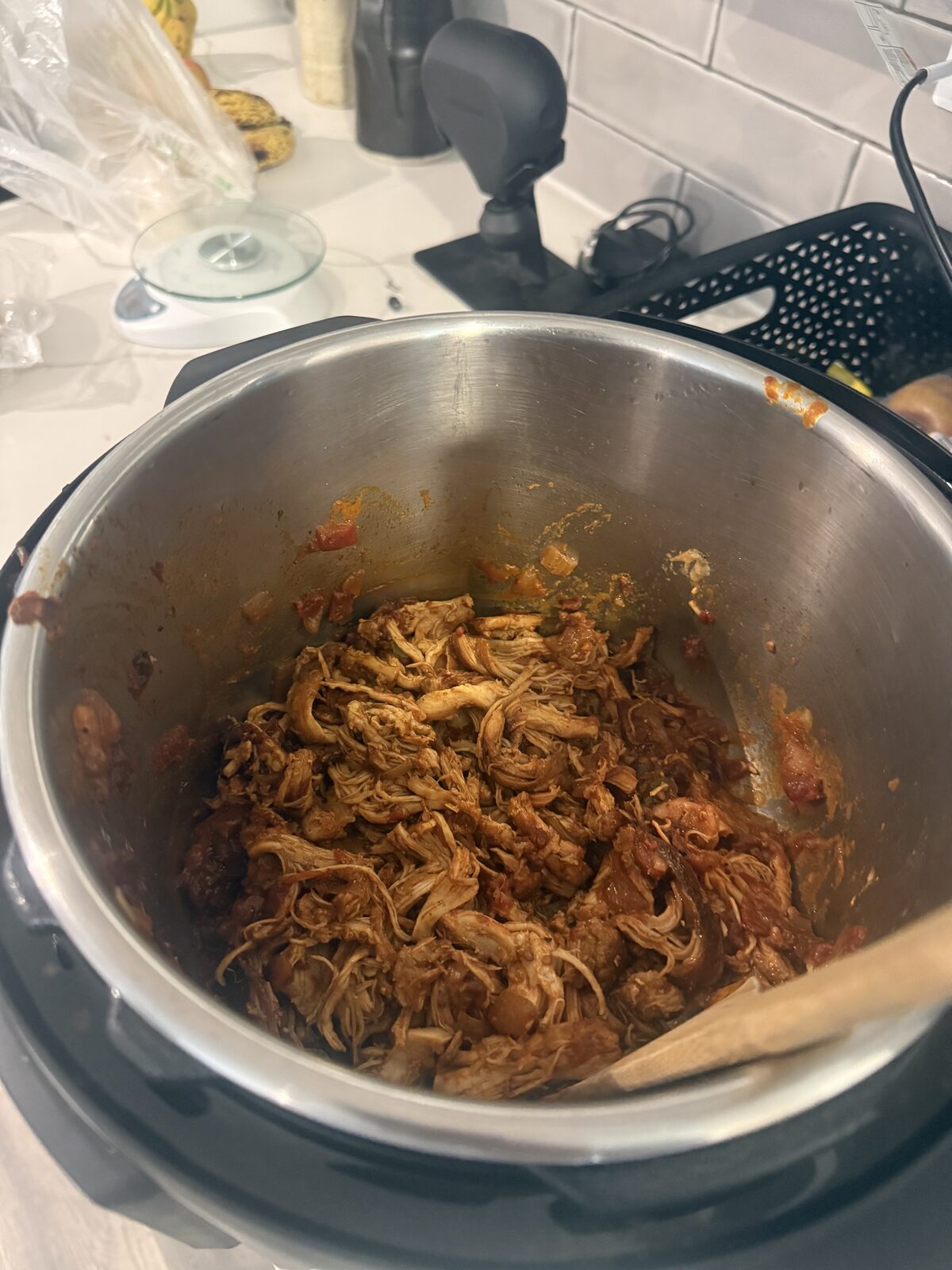 Shredded chicken tinga in the Instant Pot, glossy with chipotle-tomato sauce and a wooden spoon