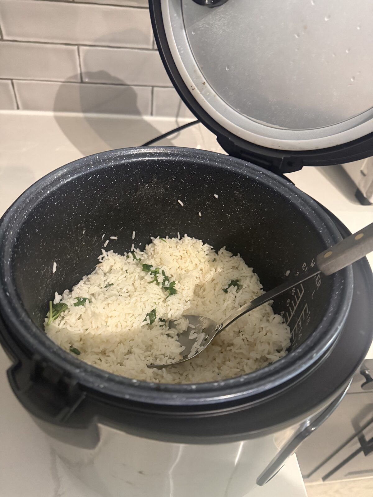Cilantro lime rice in the rice cooker pot with a fork lifting a section, fresh cilantro flecked through the grains