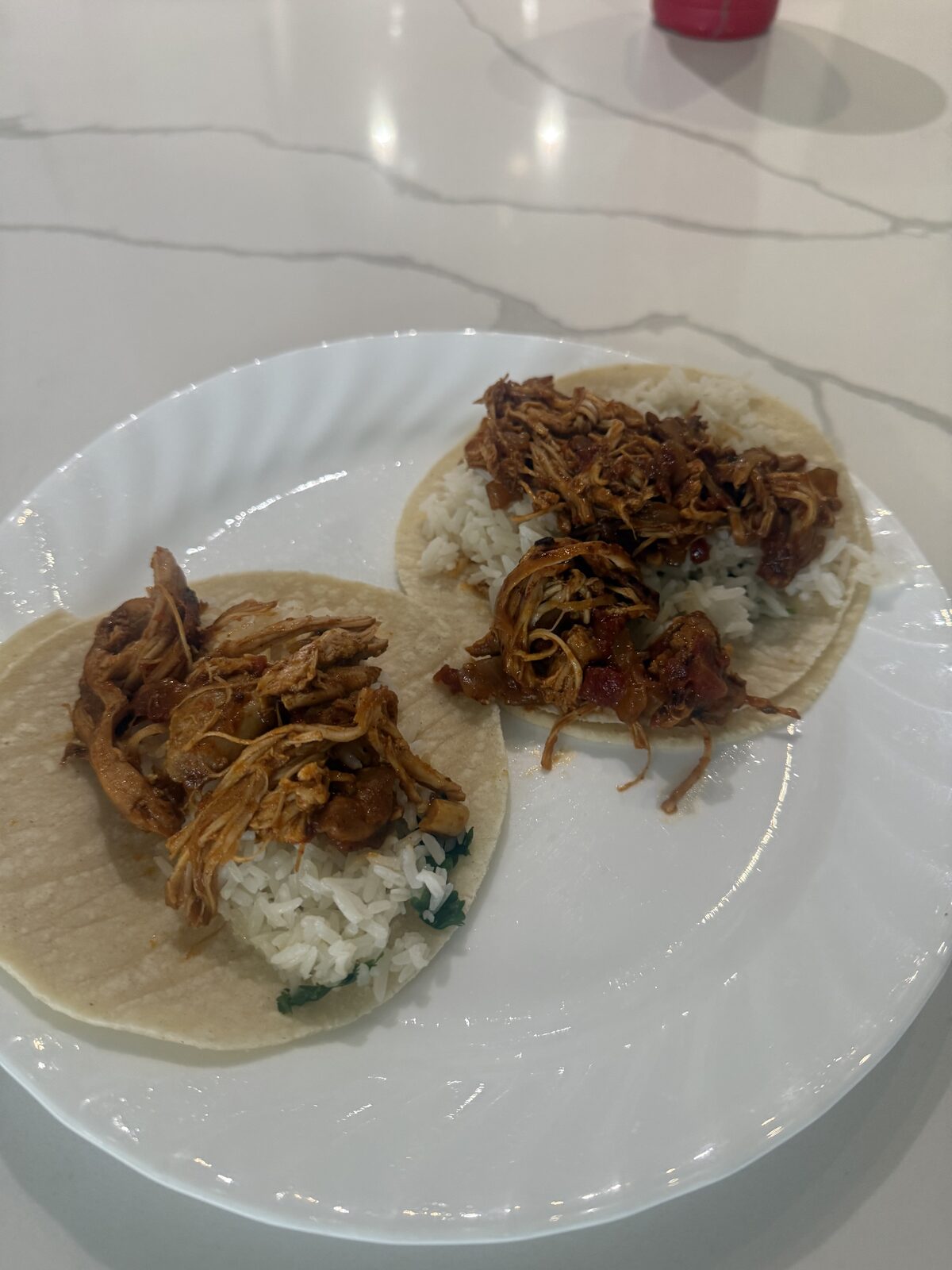 Two corn tortilla tacos on a white plate, piled with shredded chicken tinga and cilantro lime rice